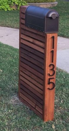 a mailbox sitting in the grass next to a sidewalk with a number on it