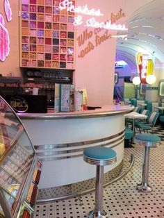 the inside of a diner with stools and tables in front of it that has neon signs on the wall