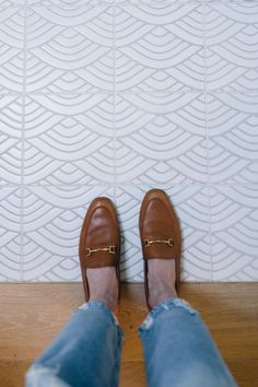 a person wearing brown shoes standing in front of a white tile wall