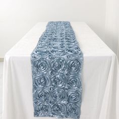 a white table with a blue rosette runner on it's end and the center piece is made out of glass