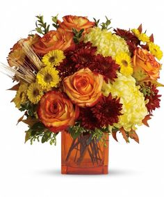 a vase filled with orange and yellow flowers on top of a wooden table next to a book