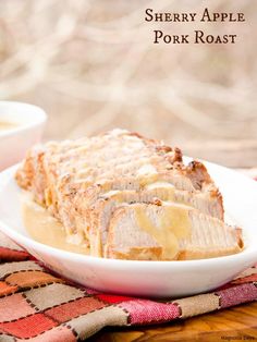 sliced pork roast on a white plate with gravy in the middle and two small bowls to the side