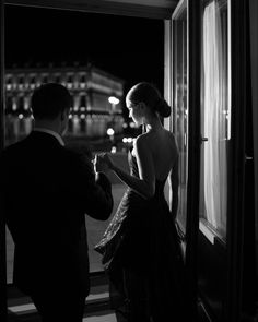 a man and woman standing next to each other in front of a window at night