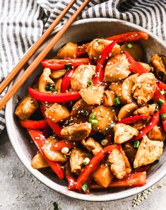 a bowl full of chicken and peppers with chopsticks on the side next to it