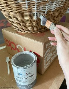 a person holding a paintbrush next to a box with a basket on top of it