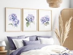 a bed with purple and white flowers on the wall next to two framed pictures above it