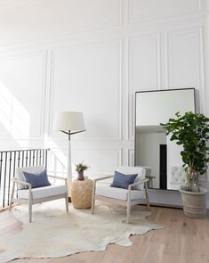 a living room filled with furniture and a mirror on top of a wooden floor next to a white wall