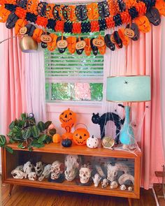 halloween decorations are displayed on a shelf in front of a window with pink drapes