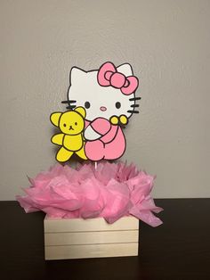 a hello kitty cake topper sitting on top of a wooden box with pink tissue