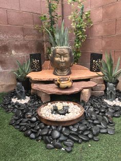 a buddha statue sitting on top of a wooden table surrounded by rocks and succulents