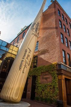 a giant baseball bat sitting in front of a tall brick building with ivy growing on it's sides