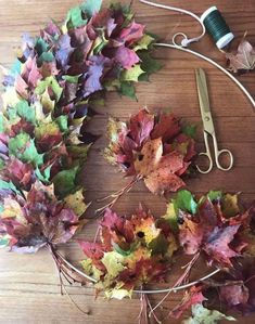 a pair of scissors sitting on top of a wooden table next to leaves and yarn