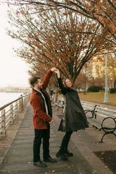 a man and woman standing next to each other in front of a tree with leaves on it