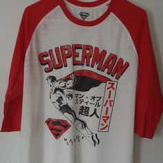 a white and red shirt with the words superman printed on it's chest is hanging up against a wall