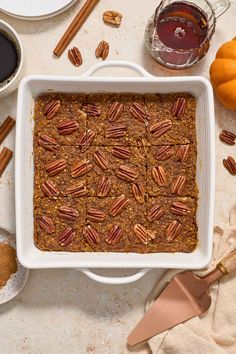 a white casserole dish filled with granola and pecans on top of a table