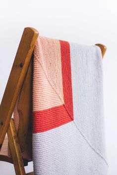 a wooden chair with a knitted blanket on it's back, sitting in front of a white wall