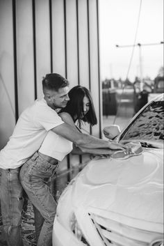 a man and woman are washing the hood of a white car in black and white