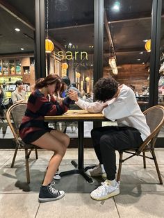 a man and woman sitting at a table in front of a store window playing with each other