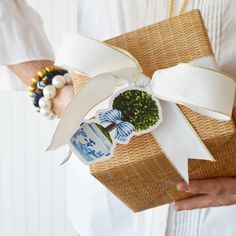 a person holding a gift wrapped in white ribbon and decorated with broccoli on it