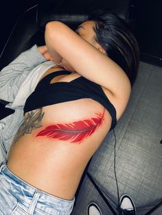 a woman laying on top of a couch next to a black chair with a red feather tattoo on her stomach