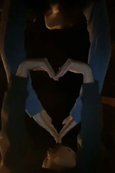 two hands making a heart shape with their fingers in the dark, while another person holds out their hand