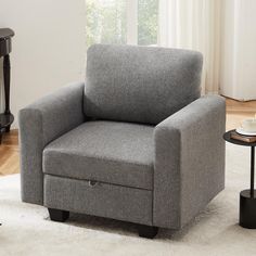 a gray chair sitting on top of a white rug next to a table and window