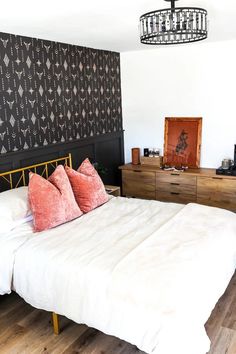 a white bed sitting next to a wooden dresser under a light hanging from a chandelier