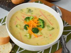 a white bowl filled with broccoli and carrots next to a slice of bread