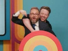 two men are hugging each other in front of a colorful wall with circles on it