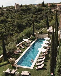 an aerial view of a pool surrounded by trees and lawn chairs with people in it