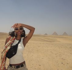 a woman standing in the desert with her hands on her head and two pyramids in the background