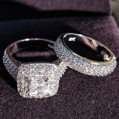 two wedding rings sitting on top of a purple velvet covered cushion with diamonds surrounding them