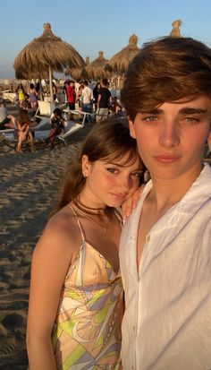 two people standing next to each other on a beach with umbrellas in the background