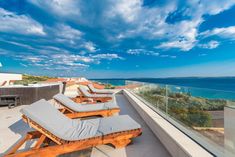 two lounge chairs sitting on top of a balcony next to the ocean with blue sky and clouds