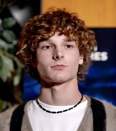 a young man with curly hair wearing a necklace