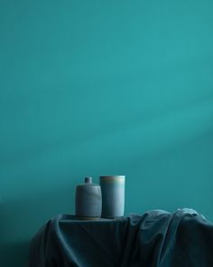 two vases sitting on top of a table covered by a blue sheet in front of a green wall