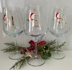 three wine glasses sitting on top of a table next to evergreen branches and pine cones