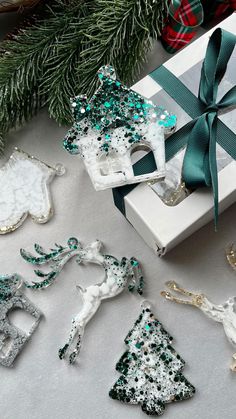 christmas ornaments are sitting on a table next to a gift box and green ribbon tied around it