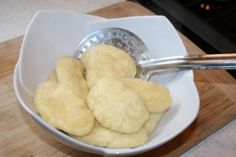 a white bowl filled with dumplings on top of a wooden cutting board next to a stove