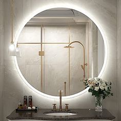 a bathroom sink with a round mirror above it and flowers on the counter top in front of it