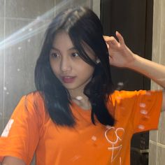 a woman in an orange shirt is holding her hair up and looking at the camera