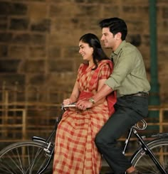 a man riding on the back of a bike next to a woman in a red and yellow dress