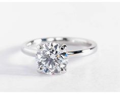 a round brilliant cut diamond engagement ring on a plain white surface with the center setting in 18k white gold