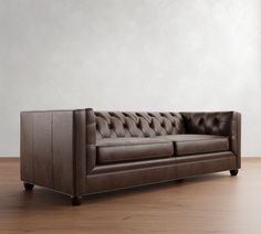 a brown leather couch sitting on top of a wooden floor next to a white wall