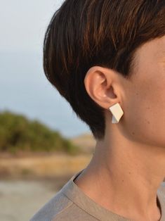 a woman with short brown hair wearing white earring and looking off into the distance