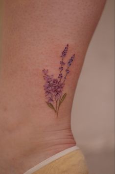 a small tattoo with purple flowers on the side of her leg and behind her is a yellow shirt