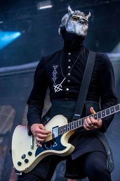 a man in a black outfit with a white guitar and wearing a horned mask on his head