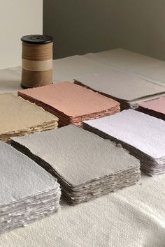 several different colors of paper on a table next to a spool of thread and a cup of coffee