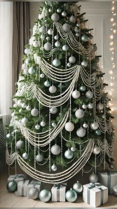 a christmas tree decorated with silver and white balls, pearls and beads is surrounded by presents