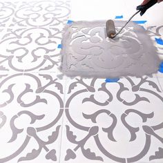 a person is using a paint roller to paint a tile floor with white and gray designs